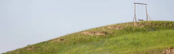 Деревянные качели на зеленом холме под ясным небом, баннер — стоковое фото