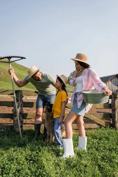 Bauer mit Rechen spricht mit Tochter neben lächelnder Frau und Rinderhund — Stockfoto