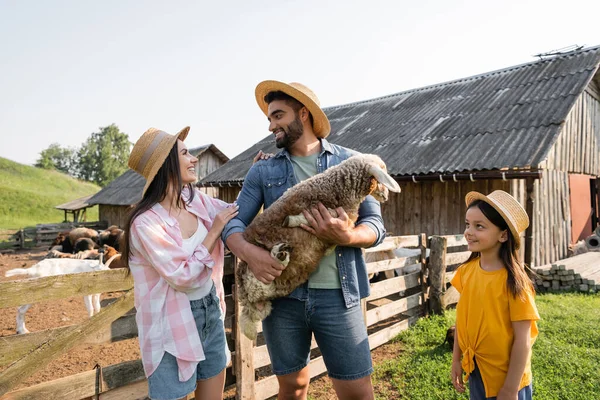 Glückliche Frau sieht Ehemann mit Lamm auf Rinderfarm stehen — Stockfoto