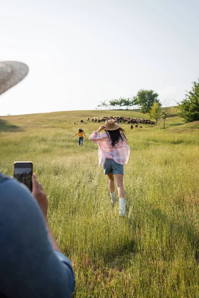 Расплывчатый мужчина фотографирует жену и дочь, бегущих по зеленым лугам в сельской местности — стоковое фото