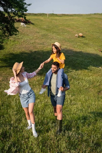 Smiling farmer piggybacking daughter near wife on farmland in countryside — Stock Photo
