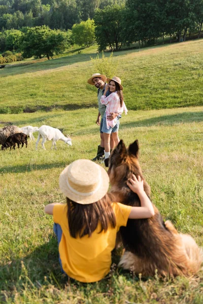 Fermiers heureux dans des chapeaux de paille élevage près de fille floue avec chien de bétail — Photo de stock