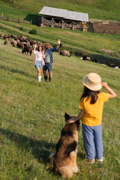 Happy farmers waving hands to daughter with dog while herding cattle in pasture — Stock Photo