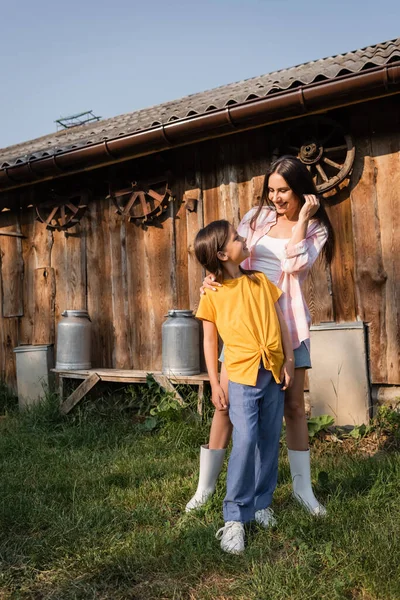 Longitud completa de la mujer y la niña mirándose el uno al otro cerca de granero de madera en la granja - foto de stock