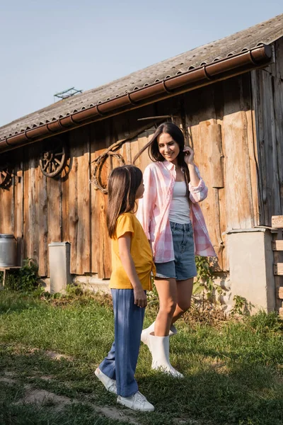 Longitud completa de la mujer sonriente hablando con su hija en la granja en el campo - foto de stock
