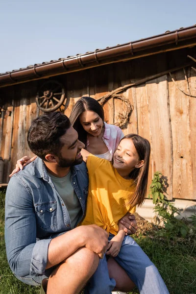 Familia alegre abrazándose y mirándose en la granja del pueblo - foto de stock