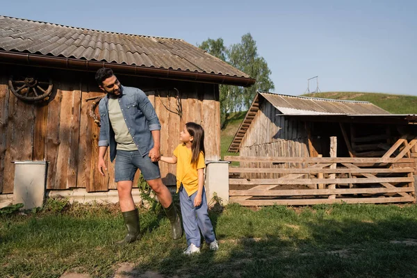 Piena lunghezza del padre e della figlia che si tengono per mano mentre camminano in fattoria — Foto stock