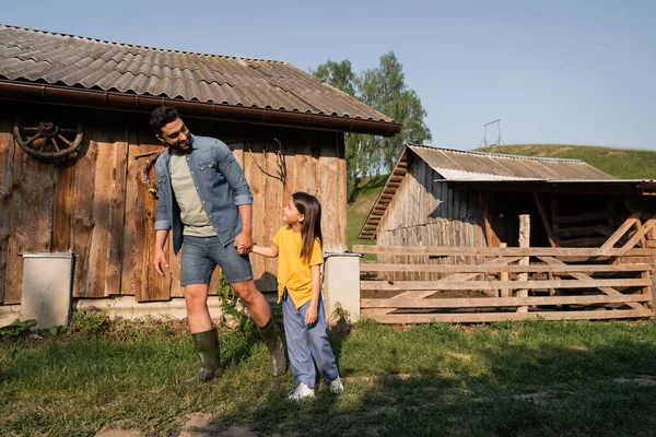 Full length of father and daughter holding hands while walking on farm - foto de stock