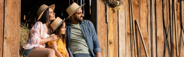 Couple of farmers and girl in straw hats looking away near wooden barn, banner — Stockfoto