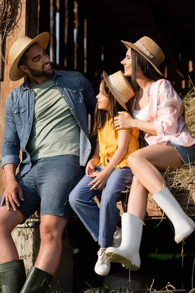 Fröhliches Paar mit Strohhüten schaut sich bei Tochter auf Heu in Scheune an — Stockfoto