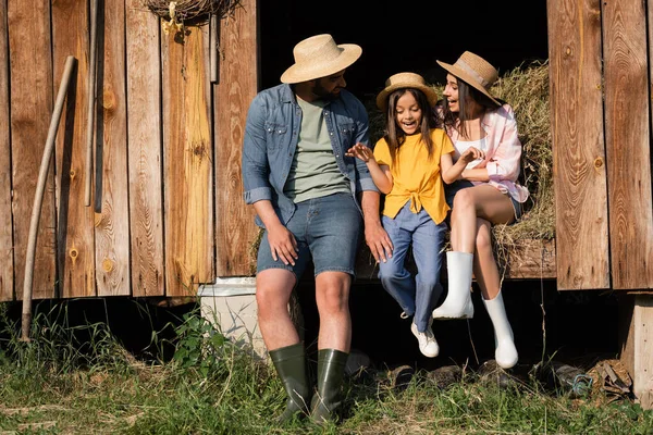 Happy child in straw hat talking near parents on hay in wooden barn — Photo de stock
