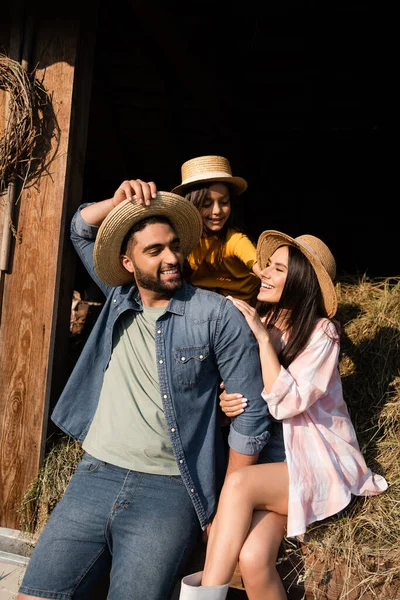 Homem feliz ajustando chapéu de palha perto da família na fazenda rural — Fotografia de Stock