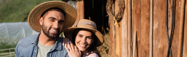 Cheerful couple of farmers in straw hats smiling at camera on family farm, banner - foto de stock