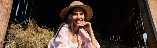 Femme gaie en chapeau de paille regardant la caméra près de la meule de foin dans la grange, bannière — Photo de stock