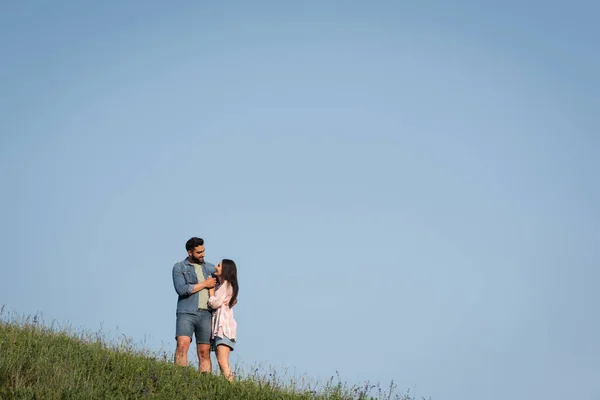 Romantisches Paar schaut einander an und umarmt sich im Feld unter blauem Himmel — Stockfoto