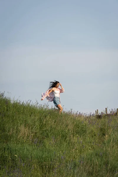 Возбужденная женщина бежит в травянистом поле с полевыми цветами в летний день — стоковое фото