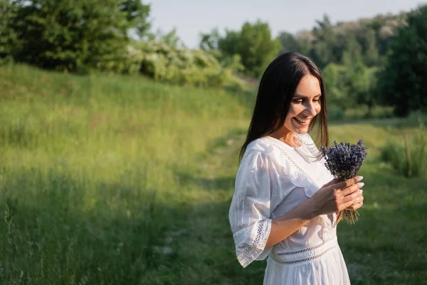 Pleased woman looking at bouquet of lavender in countryside on blurred background — Fotografia de Stock