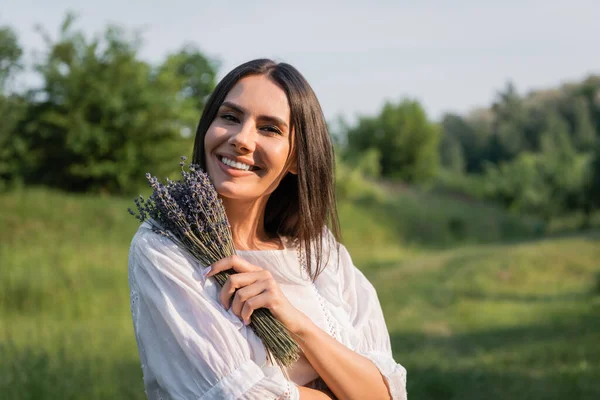 Happy brunette woman with bouquet of lavender looking at camera outdoors — Photo de stock
