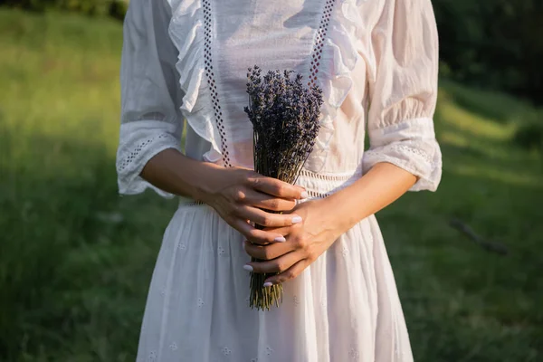 Cropped view of woman in white dress with bouquet of lavender on blurred background — Photo de stock