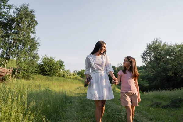 Mother and child holding hands and smiling at each other while walking in countryside — Foto stock