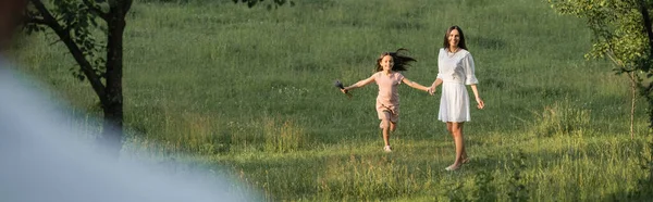 Excited girl holding hands with mother while walking in field, banner - foto de stock