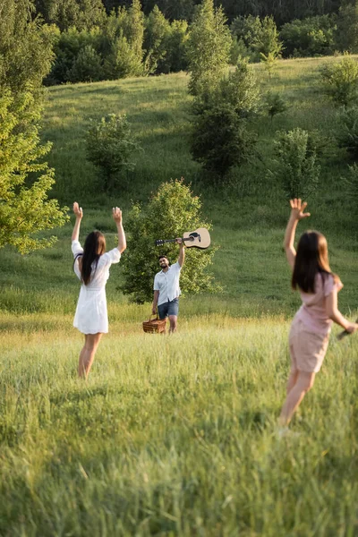 Mom and daughter waving hands to man with guitar on picturesque slope — Foto stock