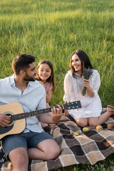 Homem tocando guitarra para a família feliz durante o piquenique de verão no campo — Fotografia de Stock