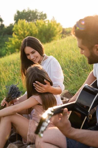 Размытый мужчина играл на гитаре рядом с женой и дочерью в летний день — стоковое фото
