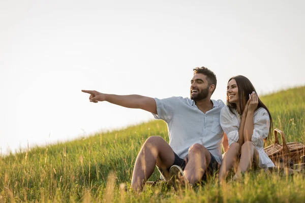 Cheerful bearded man pointing away near smiling woman in green meadow — Stock Photo