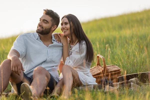 Glückliche brünette Frau stützt sich auf die Schulter eines Mannes bei einem Picknick auf einer Wiese — Stockfoto