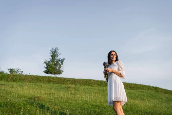 Lächelnde Frau mit Lavendelstrauß blickt in grüne Wiese — Stockfoto