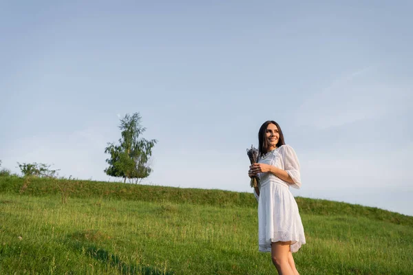 Smiling woman with lavender bouquet looking away in green meadow — Stock Photo