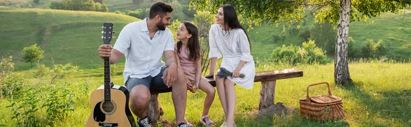 Homme heureux avec guitare parler à la fille sur le banc près de la femme avec bouquet de lavande, bannière — Photo de stock