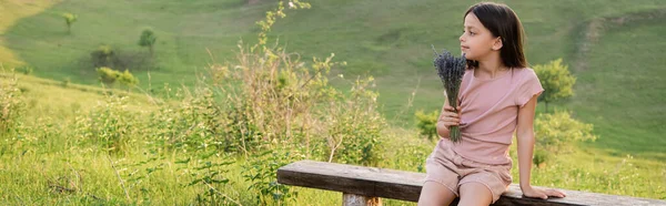 Brunette girl with lavender flowers sitting on bench in green meadow, banner — Foto stock