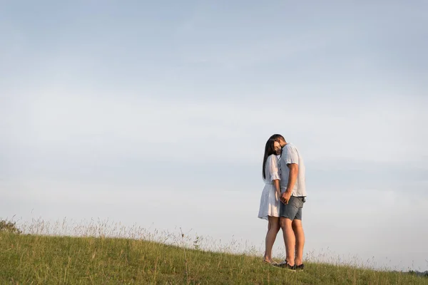 Full length of couple standing face to face and holding hands in field on summer day — Stockfoto