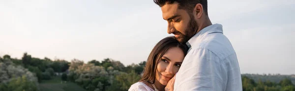 Brunette femme penché sur l'homme barbu et souriant à l'extérieur, bannière — Photo de stock