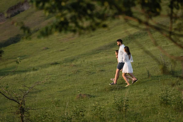 Vista laterale della famiglia che cammina in un campo verde con primo piano sfocato — Foto stock