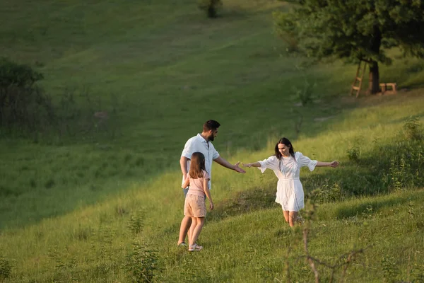 Femme tendre la main tout en courant sur la pente herbeuse vers la famille — Photo de stock