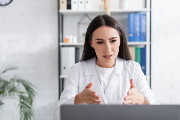 Médecin ayant un appel vidéo sur ordinateur portable flou dans la clinique — Photo de stock