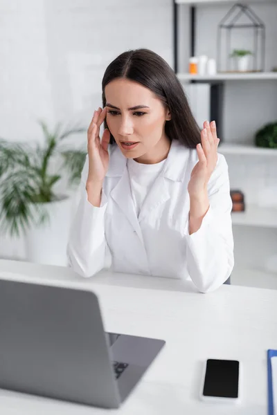 Médecin en manteau blanc ayant chat vidéo sur ordinateur portable flou à l'hôpital — Photo de stock