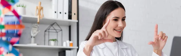 Positive doctor gesturing during online consultation on laptop in clinic, banner - foto de stock