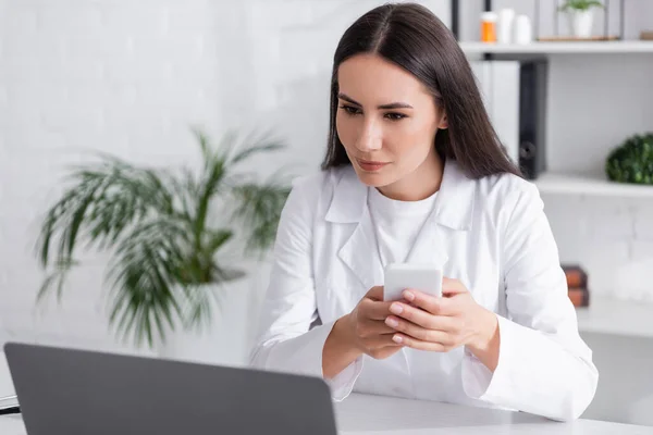 Doctor using smartphone and looking at laptop in clinic — Fotografia de Stock