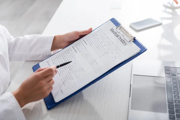 Cropped view of doctor holding medical history on clipboard near devices in clinic — Stock Photo