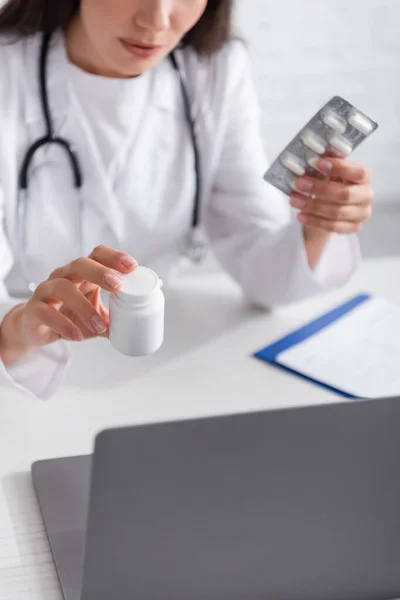 Cropped view of doctor holding pills during online consultation on laptop in hospital — Fotografia de Stock