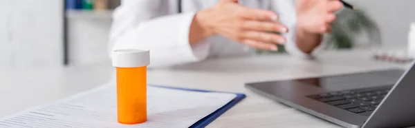 Cropped view of pills on clipboard near blurred doctor and laptop in clinic, banner — Stockfoto