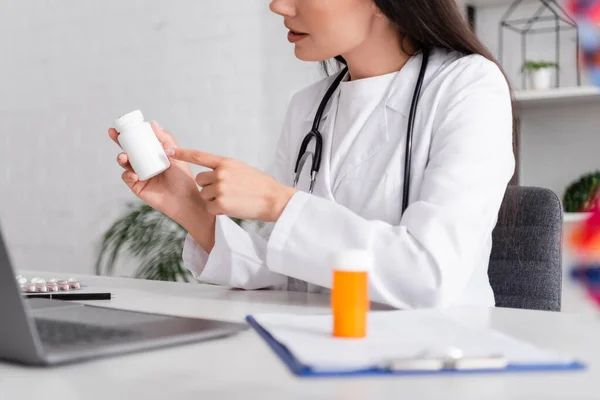 Cropped view of doctor pointing at pills during video call on laptop — Foto stock