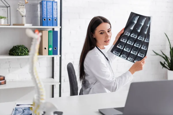 Médecin tenant le balayage IRM pendant le chat vidéo sur ordinateur portable à l'hôpital — Photo de stock