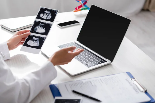 Vista ritagliata del medico in possesso di ecografia del bambino durante la consultazione online sul computer portatile in clinica — Foto stock