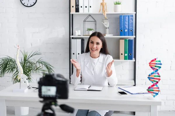 Positive doctor talking near digital camera and notebook in clinic — Stock Photo