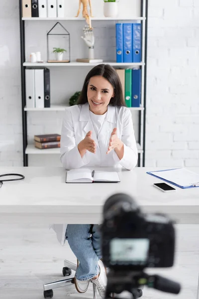 Médico sonriente hablando cerca de smartphone y cámara digital en la clínica - foto de stock